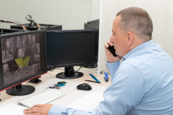 Side view of security guard watching CCTV cameras and talking on mobile phone. Surveillance, control, safety of private property concept. selective focus